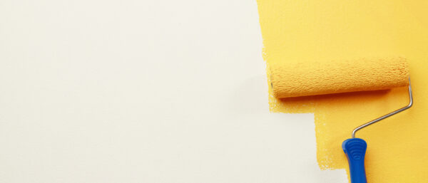 A paint roller with a blue handle is applying bright yellow paint to a white wall, partially covering the surface.